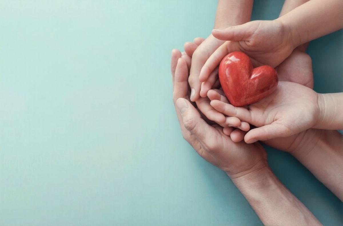 An adult's hands cradling a child's hands holding a small red heart
