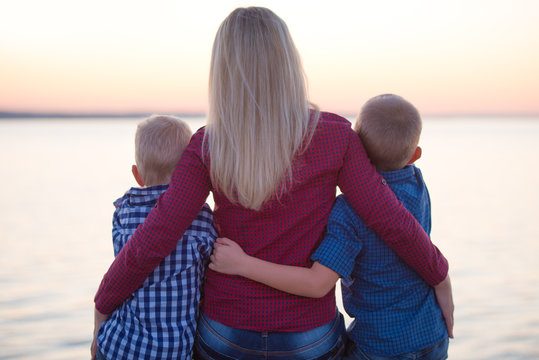 A mother with her arms around two boys, looking out at the water